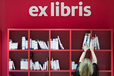 Une femme met des livres sur une étagère rouge Une femme met des livres sur une étagère rouge